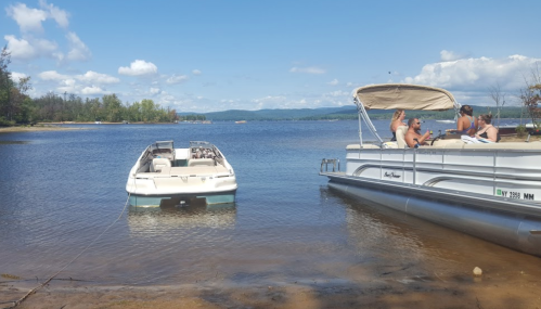 Two boats anchored in a calm lake with people relaxing on one boat under a sunny sky.