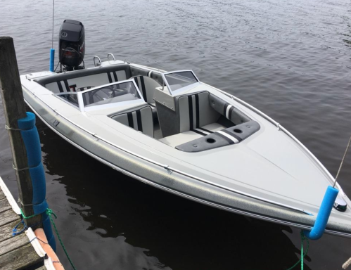 A sleek, white motorboat with gray and black seating is docked by a wooden pier on calm water.