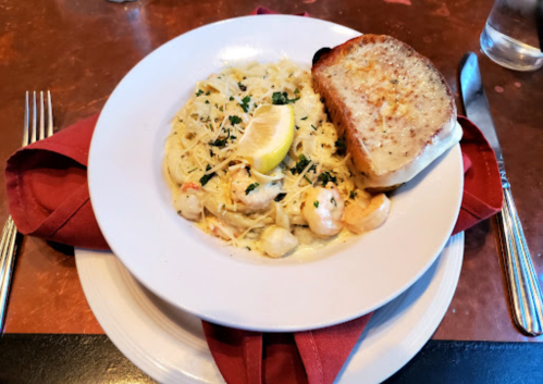 A plate of creamy pasta with shrimp, garnished with parsley and a lemon wedge, served with a slice of garlic bread.