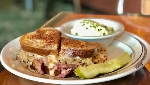 A toasted sandwich with sauerkraut and meat, served with a pickle and a side of creamy coleslaw.