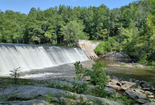 A serene view of a waterfall cascading over a dam, surrounded by lush green trees and rocky terrain.