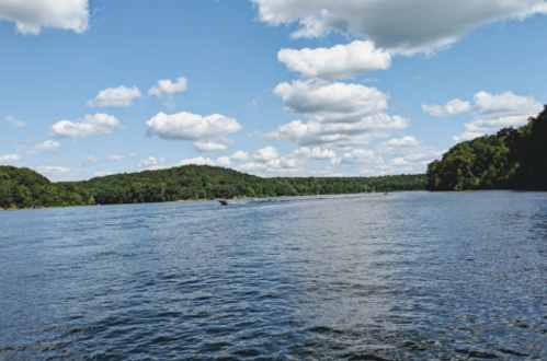 A serene river scene with lush green hills and fluffy clouds under a bright blue sky.