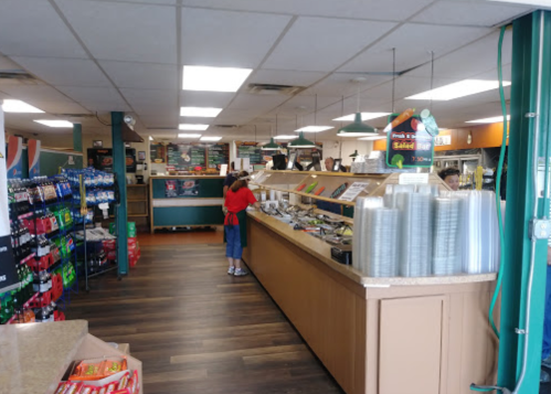 A bright deli interior with a salad bar, shelves of snacks, and a customer at the counter.