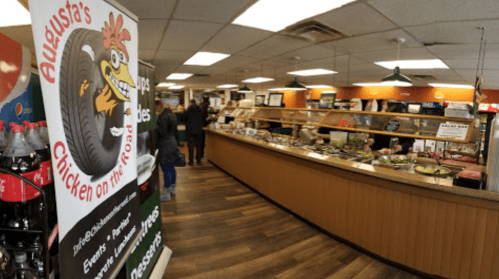Interior of a casual eatery with a buffet, featuring a colorful sign for "Augusta's Chicken on the Go." Customers are visible.