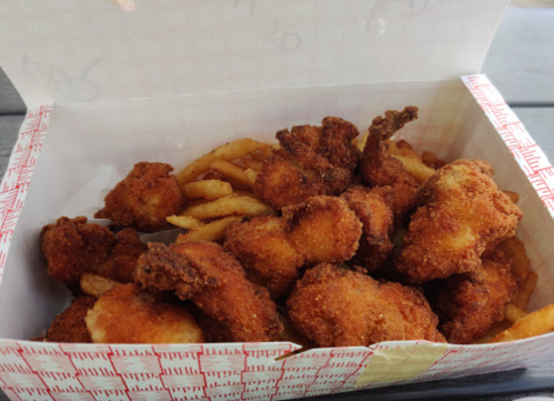 A takeout box filled with crispy fried chicken pieces and golden French fries.