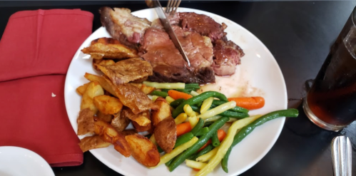 A plate of roast beef with vegetables and crispy potatoes, accompanied by a drink.
