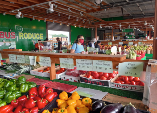 A vibrant produce market with colorful fruits and vegetables displayed on wooden tables. Shoppers browse the selection.