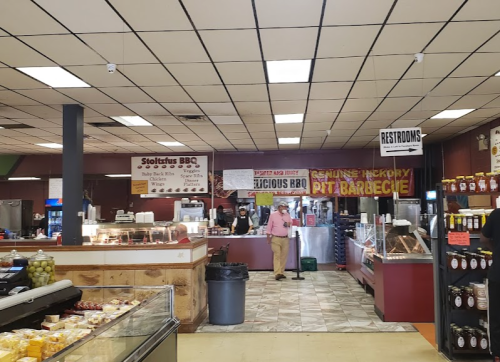 Interior of a BBQ restaurant with a counter, menu signs, and customers. Restroom sign visible in the background.