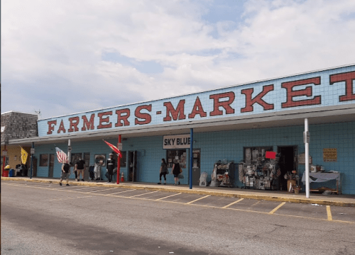 A colorful farmers market building with "FARMERS MARKET" sign, featuring shoppers and various storefronts.