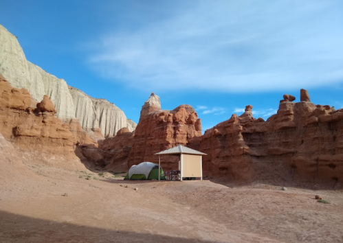 A small wooden structure and a tent nestled among red rock formations under a blue sky.