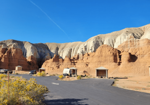 Desert landscape with colorful rock formations and small shelters along a paved road under a clear blue sky.