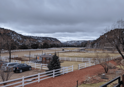 A scenic view of a ranch with white fences, mountains in the background, and overcast skies.