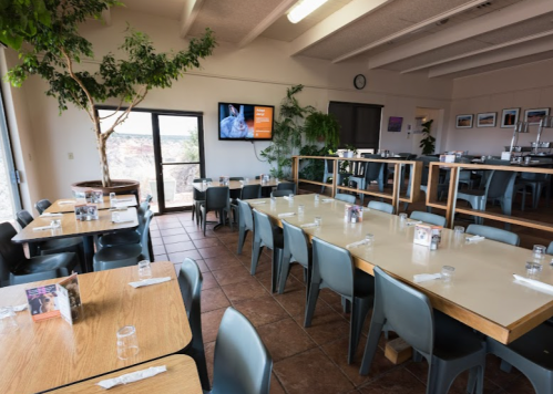 A spacious dining area with wooden tables, blue chairs, and large windows showcasing a scenic view.