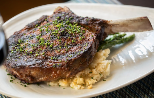 A perfectly cooked ribeye steak garnished with chives, served on a bed of creamy mashed potatoes and asparagus.