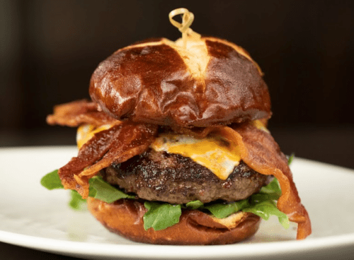 A juicy burger with bacon, cheese, and greens, served on a toasted pretzel bun.
