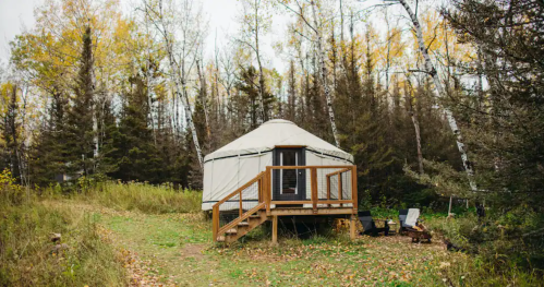 A cozy yurt on a wooden platform surrounded by trees and autumn foliage.