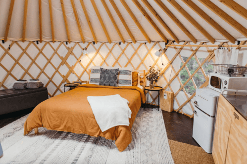 Cozy yurt interior featuring a queen bed, wooden accents, and a small kitchenette with a fridge and microwave.