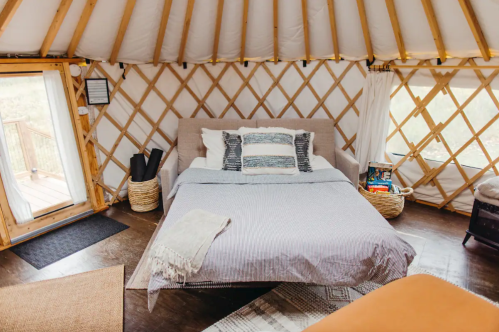 Cozy interior of a yurt featuring a bed, decorative pillows, and natural light from a nearby door.