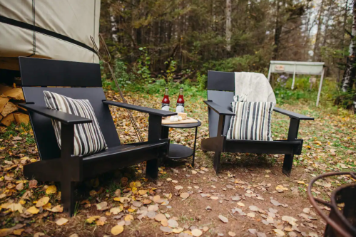 Two black outdoor chairs with striped cushions beside a small table, surrounded by autumn leaves and trees.