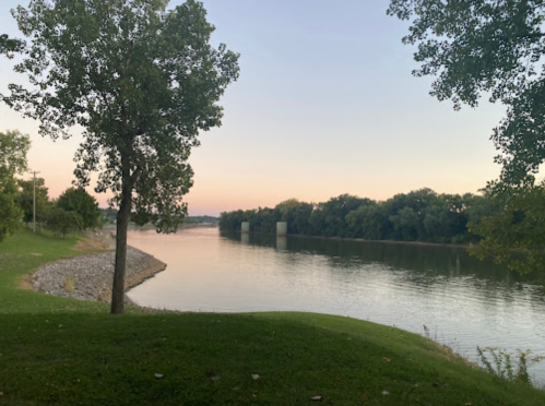 A serene river scene at dusk, with trees lining the shore and a calm water surface reflecting the soft colors of the sky.