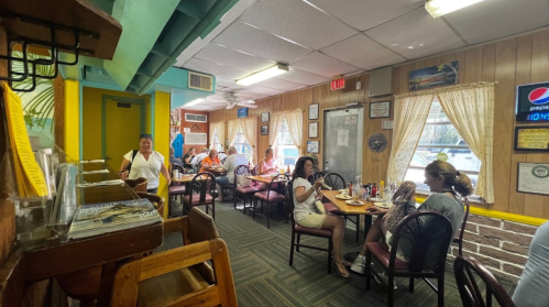 A cozy diner interior with patrons enjoying meals, wooden decor, and large windows letting in natural light.