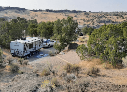 A camper and truck parked in a scenic, dry landscape with sparse trees and rocky terrain.