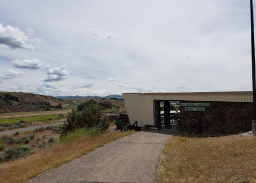 A pathway leads to a visitor center with a stone facade, surrounded by grassy hills and a cloudy sky.