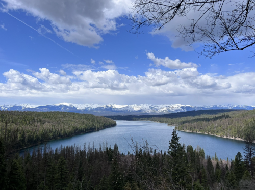 A serene lake surrounded by lush forests and snow-capped mountains under a partly cloudy sky.