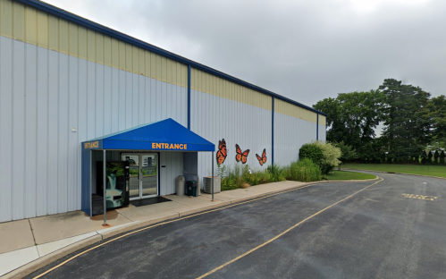 A building entrance with a blue awning, featuring butterfly murals and surrounded by greenery.