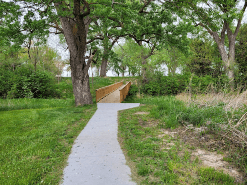 A winding path leads to a wooden bridge surrounded by lush greenery and trees.