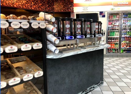 A beverage station with multiple dispensers and a display of assorted pastries in a convenience store.