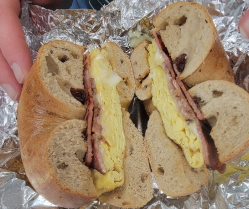 A halved bagel filled with egg, cheese, and slices of meat, wrapped in foil.