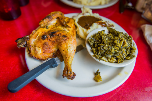 A plate featuring roasted chicken, mashed potatoes with gravy, and a side of collard greens on a red table.