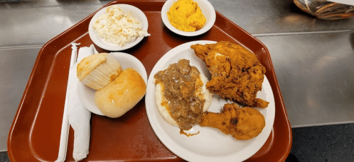 A tray with fried chicken, mashed potatoes with gravy, coleslaw, cornbread, and a muffin.