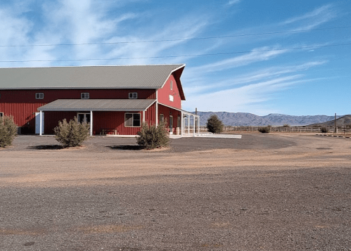 A red barn-style building sits on a gravel lot with mountains in the background under a clear blue sky.