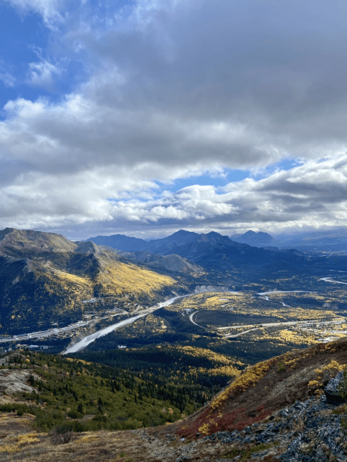 A scenic view of mountains and valleys with autumn foliage under a partly cloudy sky.
