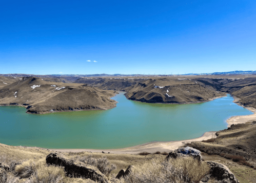 A panoramic view of a serene lake surrounded by rolling hills and clear blue skies.