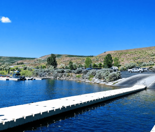 A serene lake scene with a long dock, boats, and green hills under a clear blue sky.