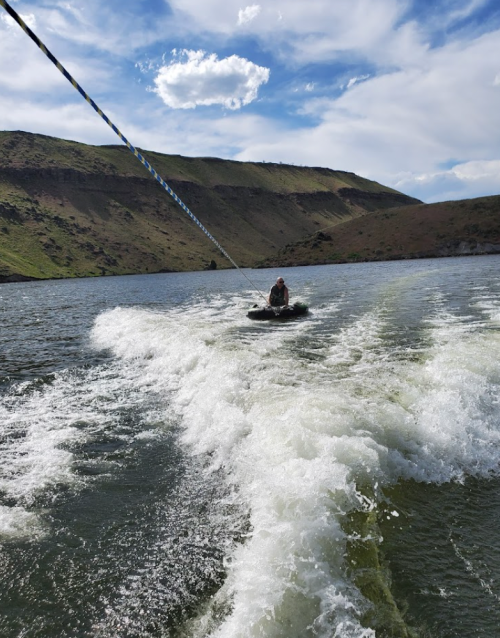 A person being towed on a wakeboard across a lake, with hills and a blue sky in the background.