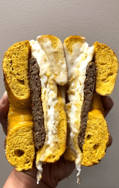 A hand holding a sandwich made with yellow bread, filled with a beef patty and melted cheese.
