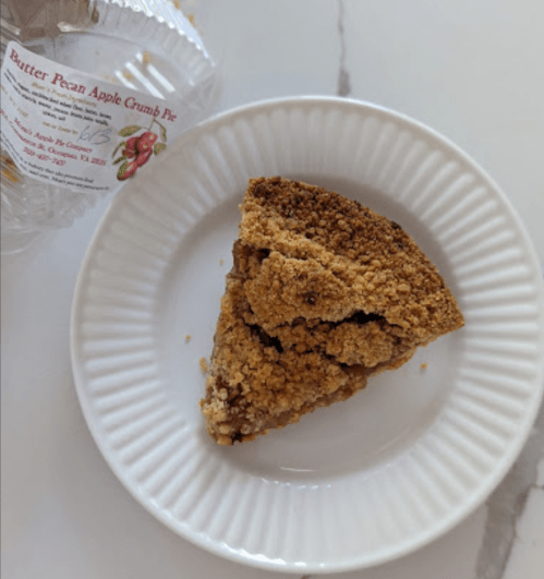 A slice of butter pecan apple crumb pie on a white plate, next to its packaging.