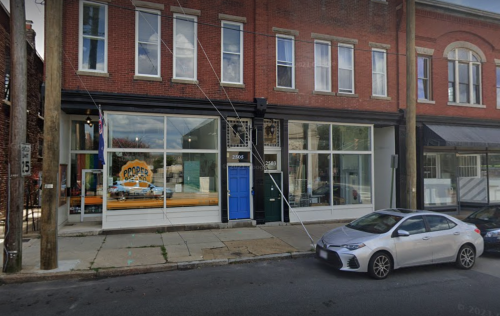 A brick building with large windows, featuring a blue door and a sign for "Proper." A parked car is in front.
