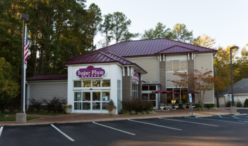 Exterior of Sugar Plum Bakery, featuring a modern building with a maroon roof, surrounded by trees and parking spaces.