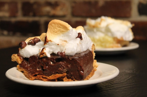 A slice of chocolate pie topped with fluffy meringue and chocolate chips, served on a white plate.