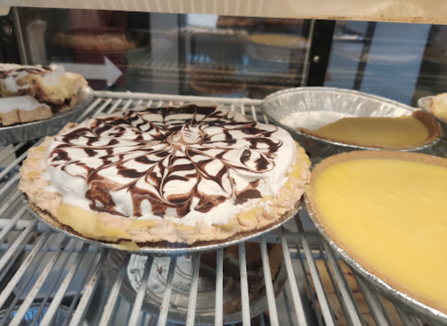 A display case with two pies: one topped with whipped cream and chocolate swirls, and a plain yellow pie.