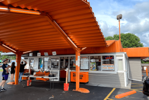 A colorful fast-food stand with an orange roof, outdoor seating, and a menu displayed on the side.