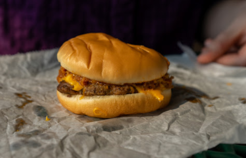 A close-up of a cheeseburger with melted cheese and crispy toppings on a crumpled paper surface.