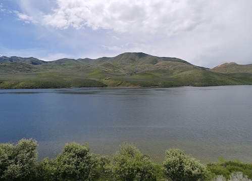 A serene lake surrounded by lush green hills under a partly cloudy sky.