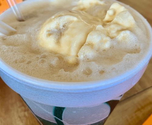 A close-up of a frothy beverage topped with scoops of ice cream in a paper cup.