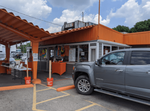 A gray truck parked outside a colorful storefront with orange awnings and a sunny sky in the background.